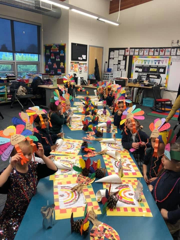 Children wearing paper turkey hats sitting at a long table in a classroom