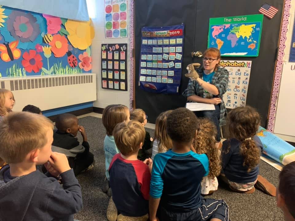 Person holding a puppet for a group of children in a classroom