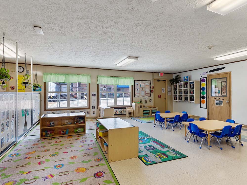 Empty classroom with small tables, chairs, and play mats