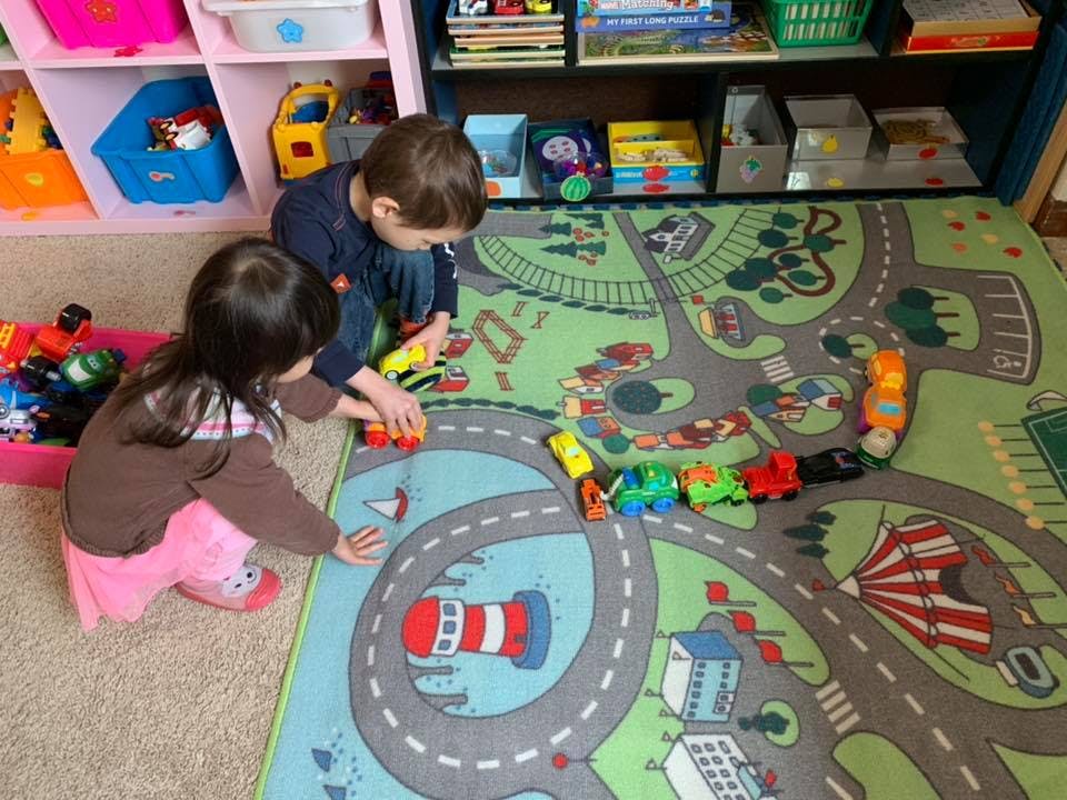 Two children playing with toy cars on a road map rug