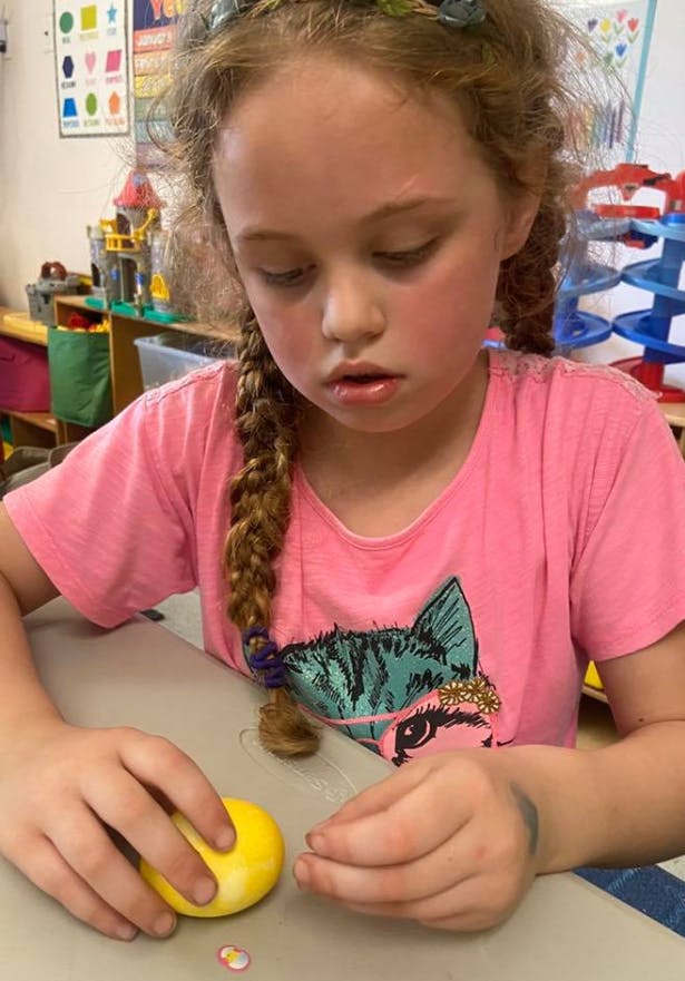 Child with braided hair decorating a yellow egg