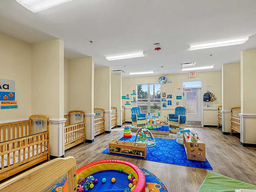 Baby room in a daycare with multiple cribs and play areas