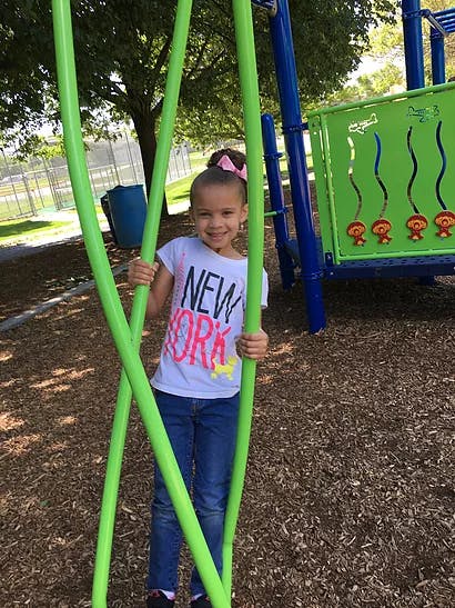 Child standing on a playground holding onto green bars