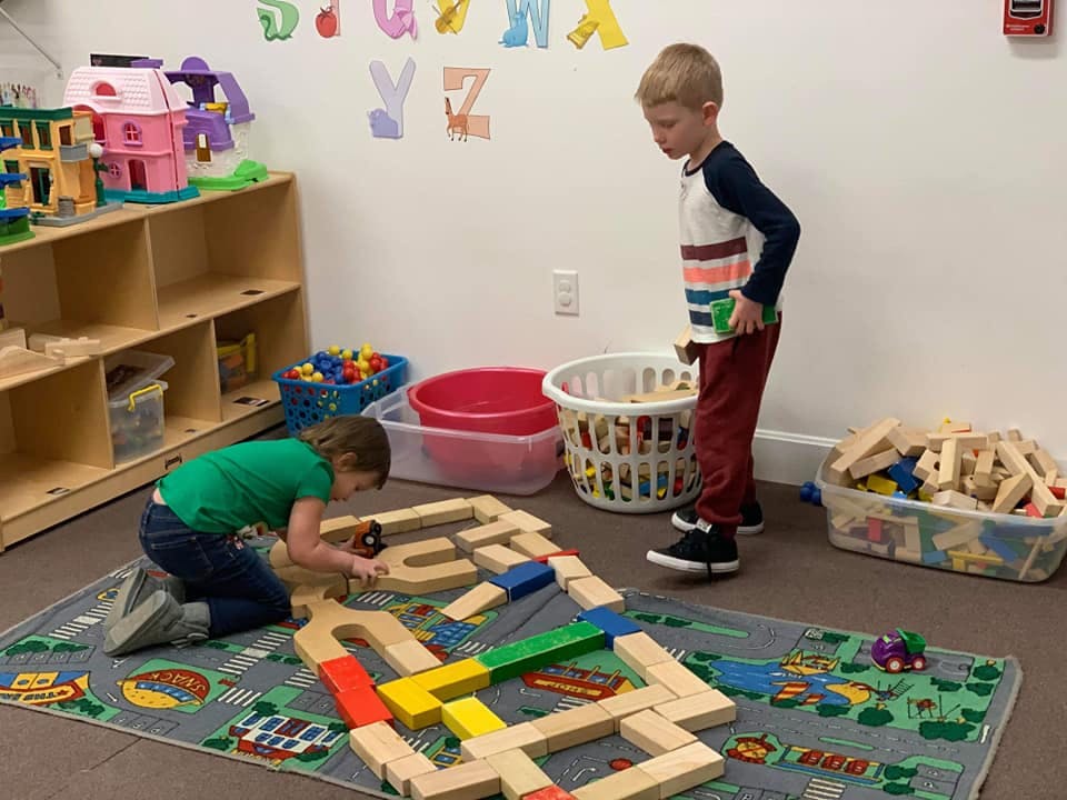 Two children playing with wooden blocks on a rug in a classroom