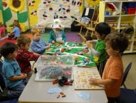 Children playing with building blocks at a table in a classroom