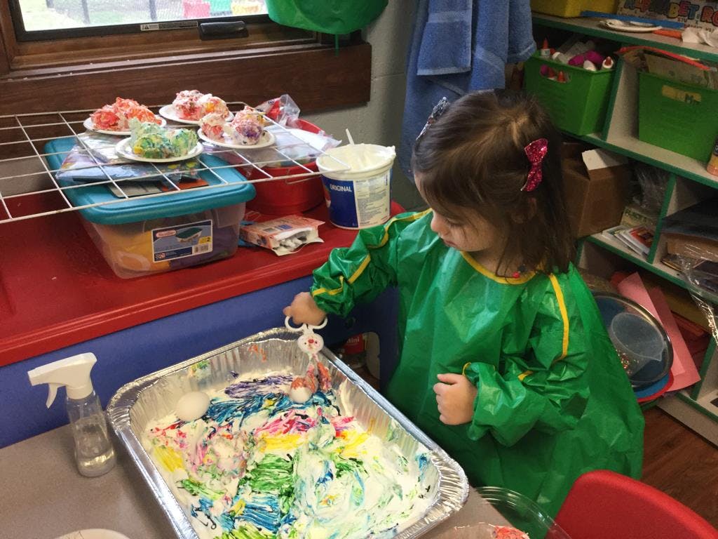 Child in a green smock playing with colorful foam in a tray