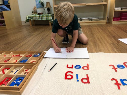 Child writing in a notebook on the floor in a classroom