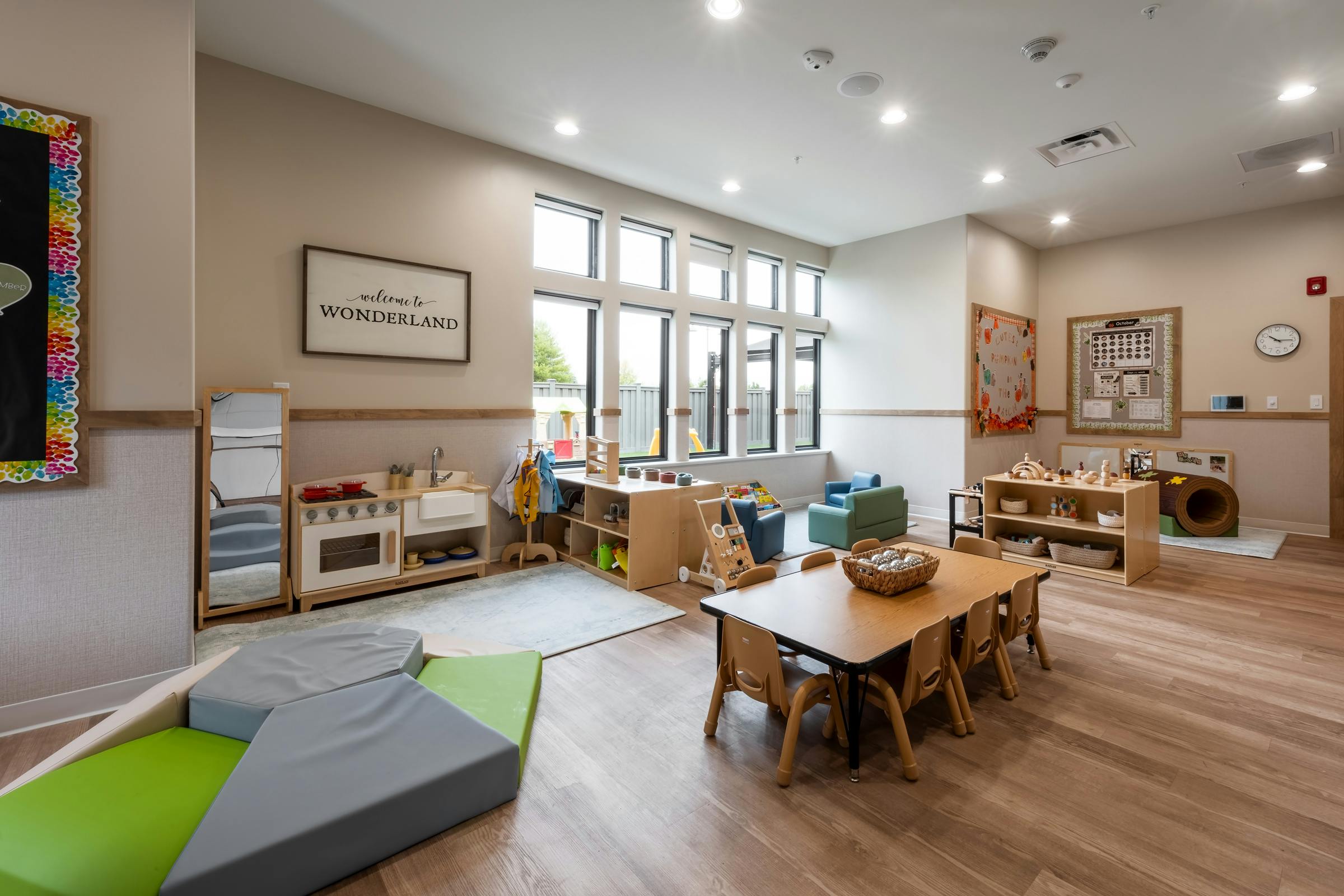 Classroom with play kitchen, tables, chairs, and large windows