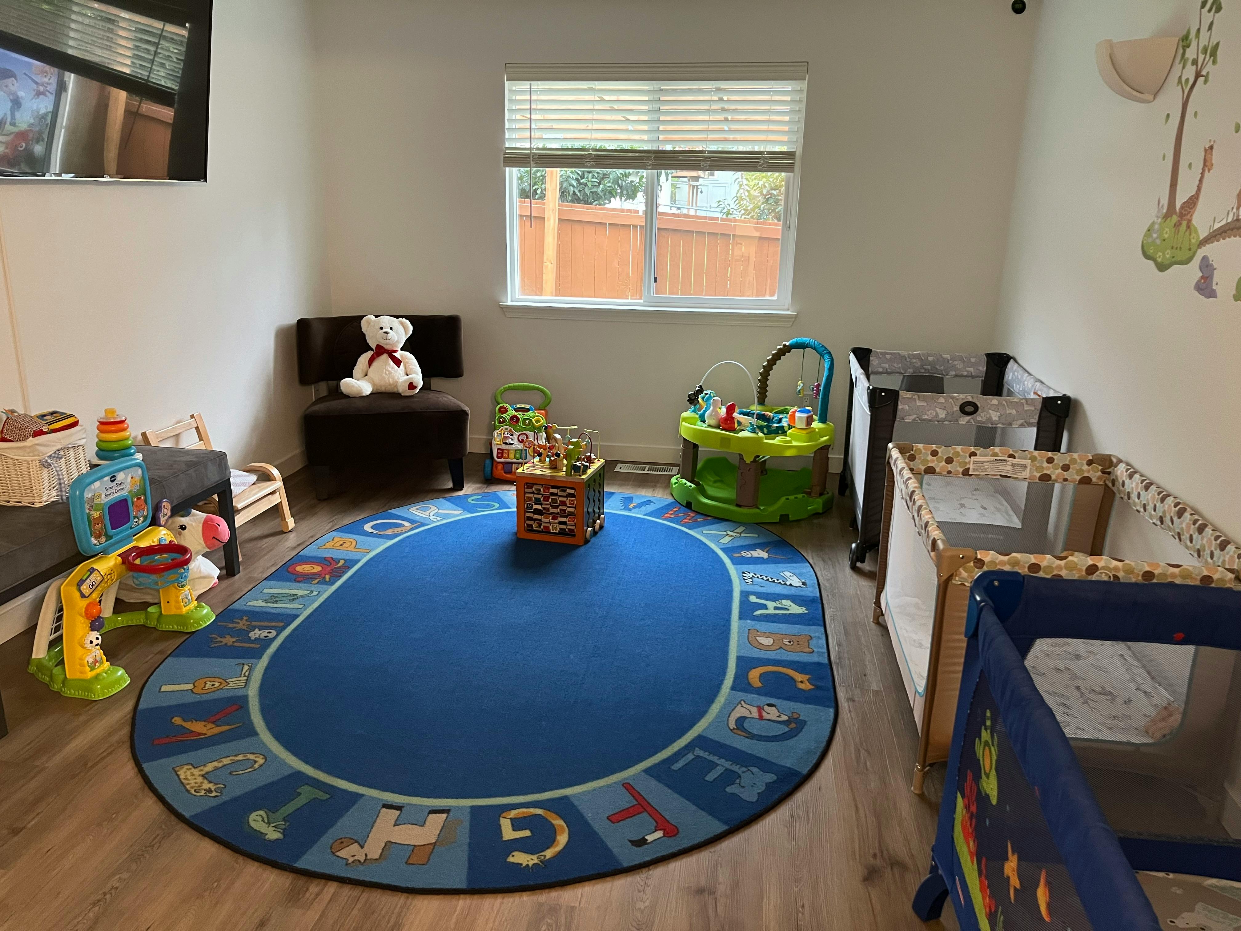 Playroom with a blue alphabet rug, playpens, and various toys