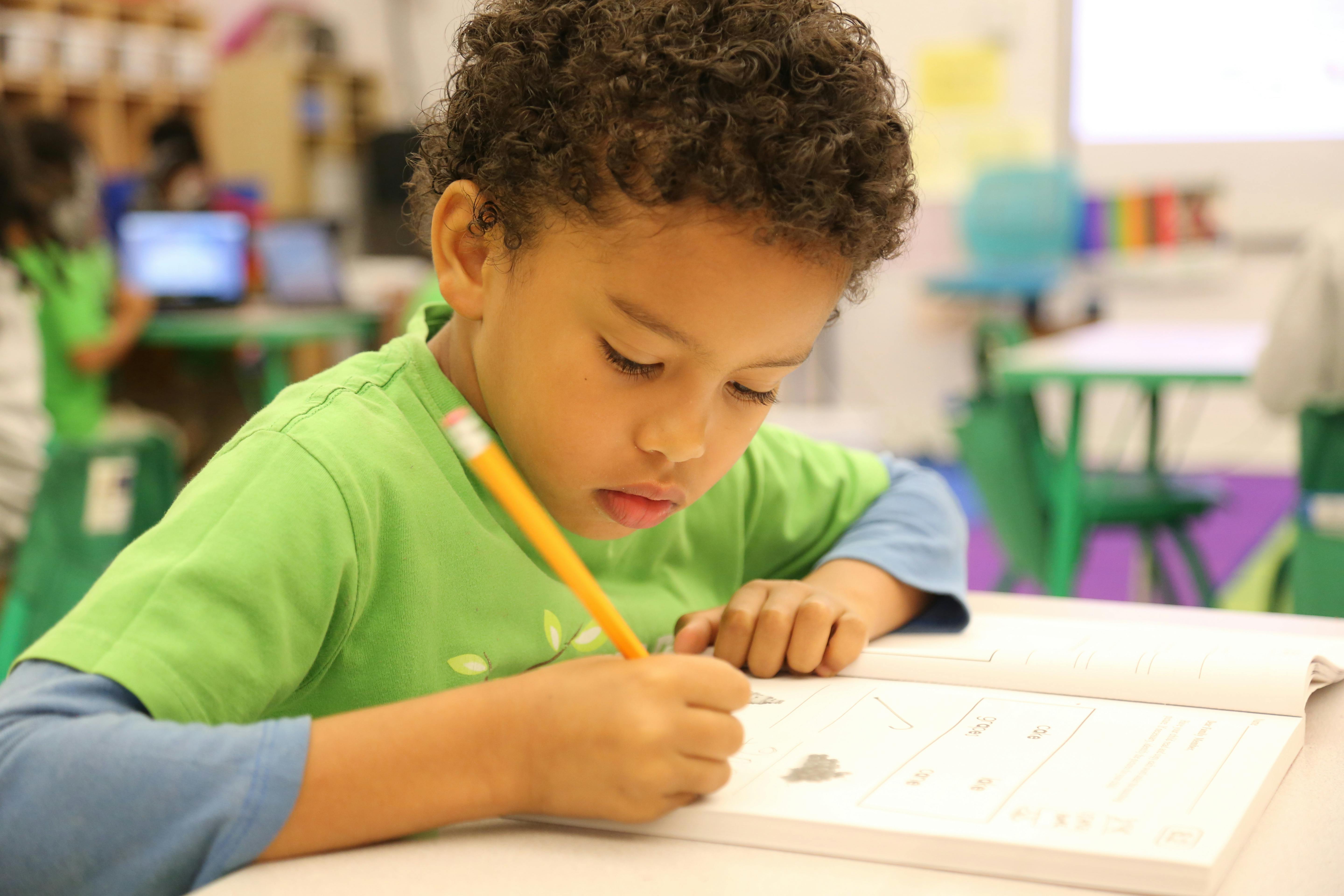 Child writing in a workbook at a desk in a classroom