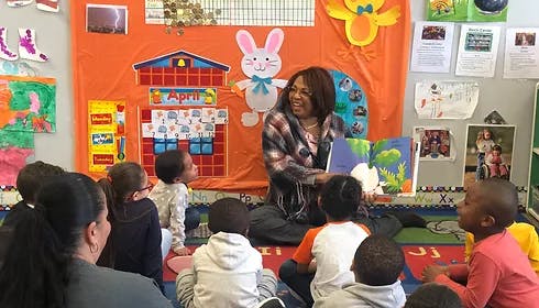 Person reading a book to a group of children in a classroom