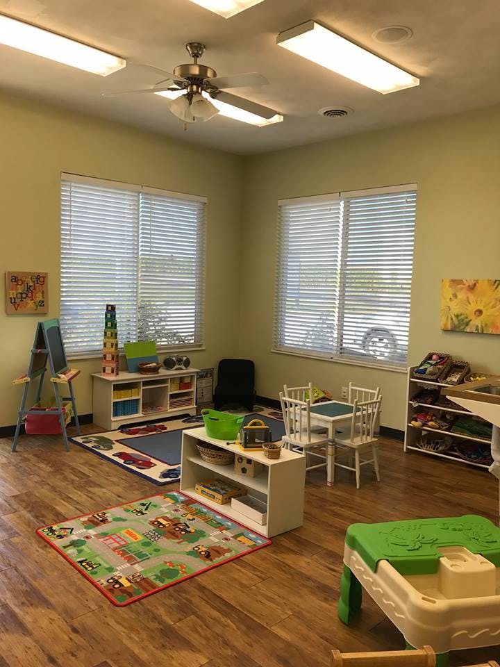 A classroom with small tables and chairs, rugs, and storage shelves
