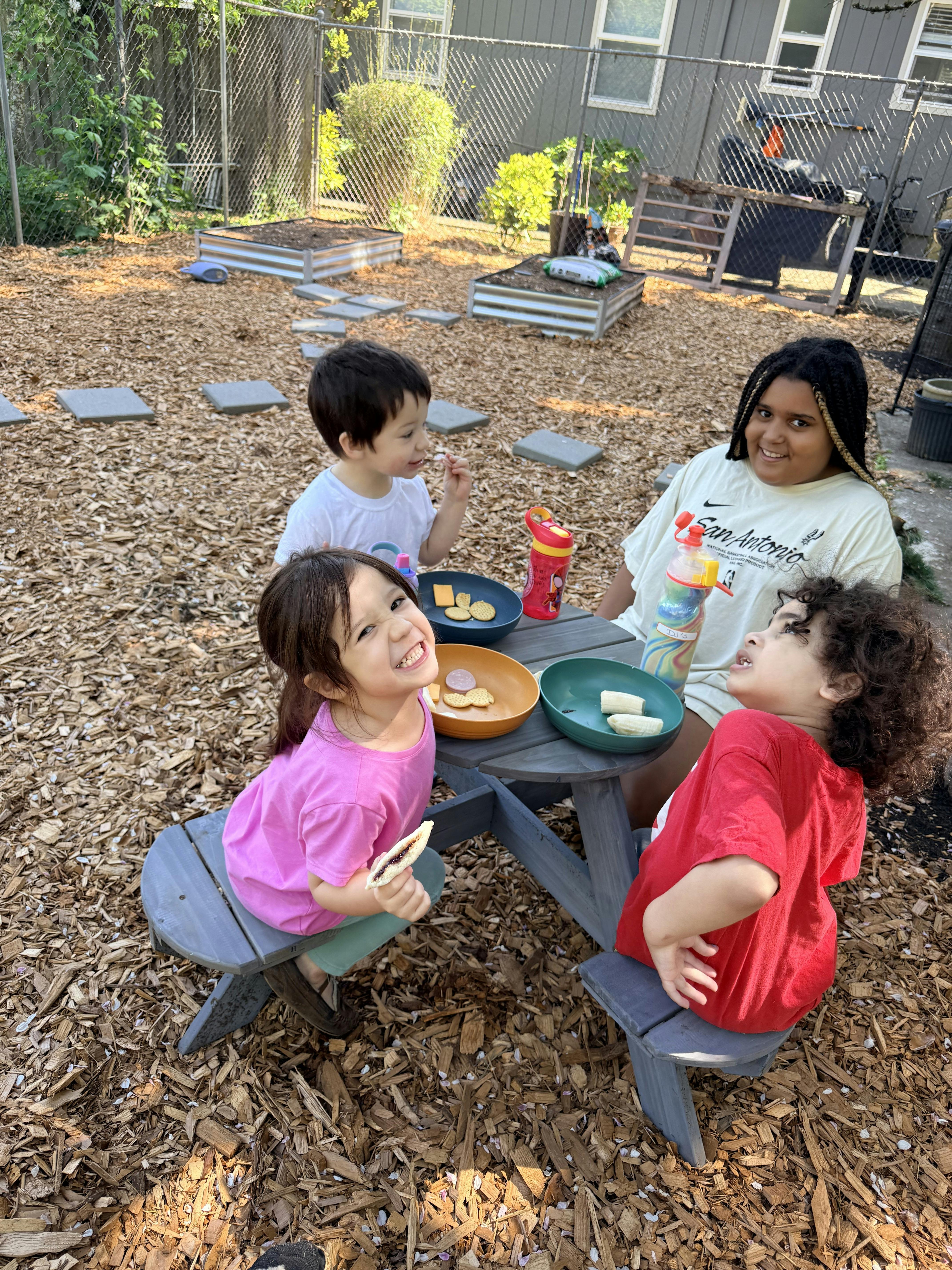 Four children sitting at a picnic table outdoors, eating snacks