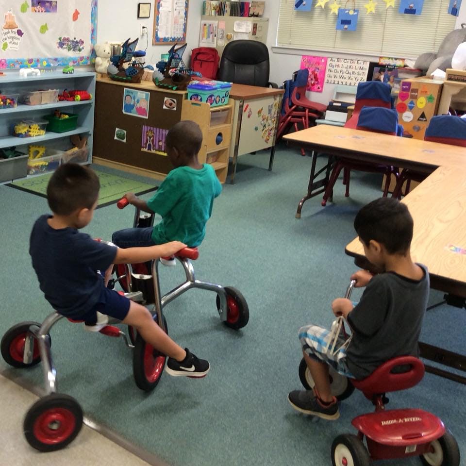 Three children riding tricycles in a classroom