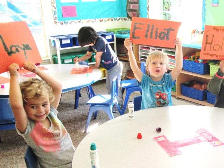 Children in a classroom holding up signs with names