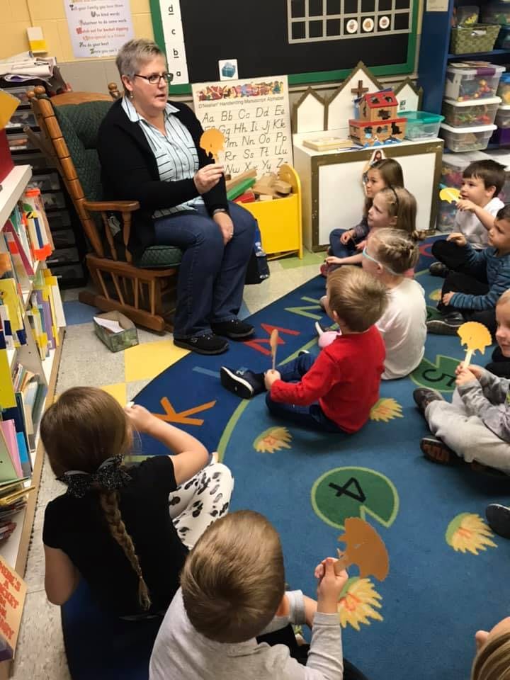 Person sitting in a rocking chair reading to children in a classroom