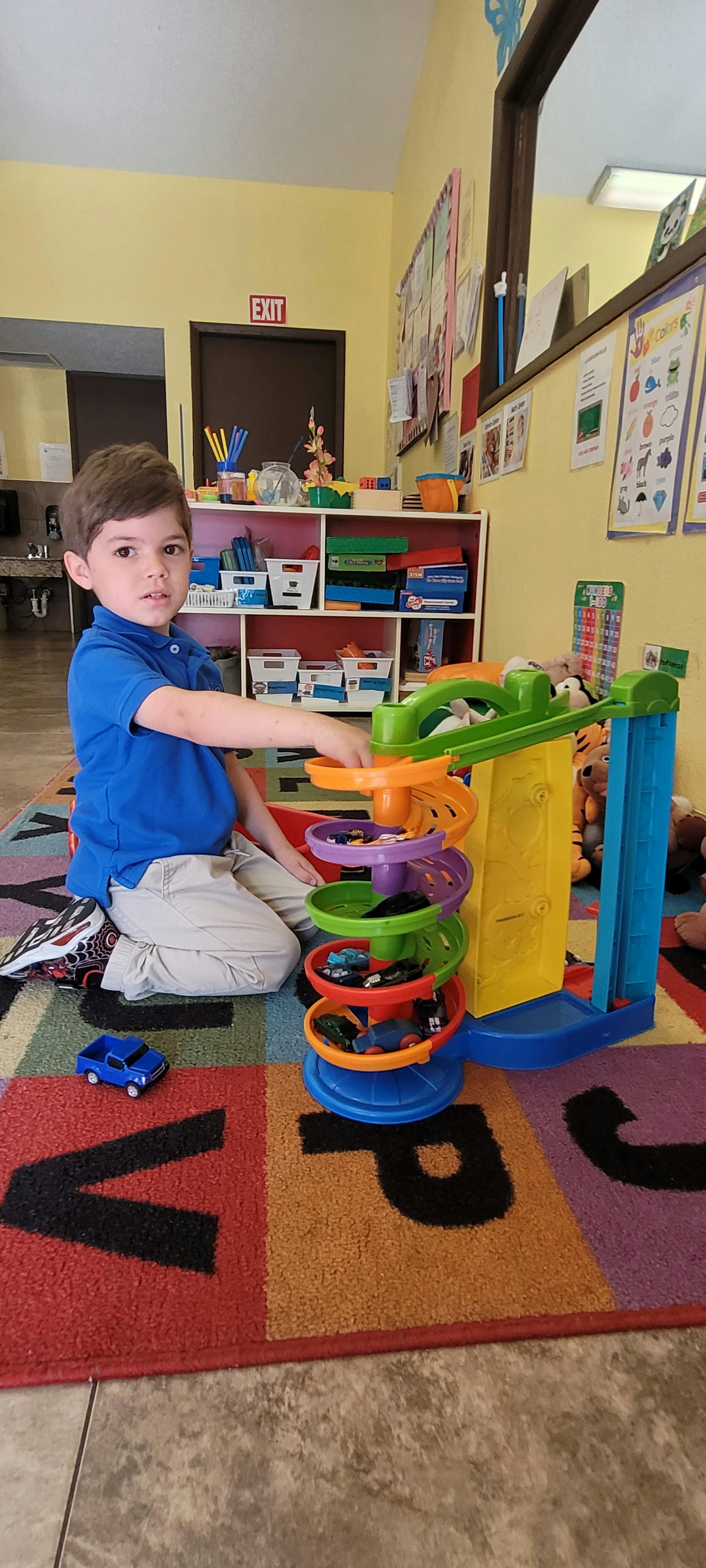 Child sitting on an alphabet rug playing with a toy spiral race track
