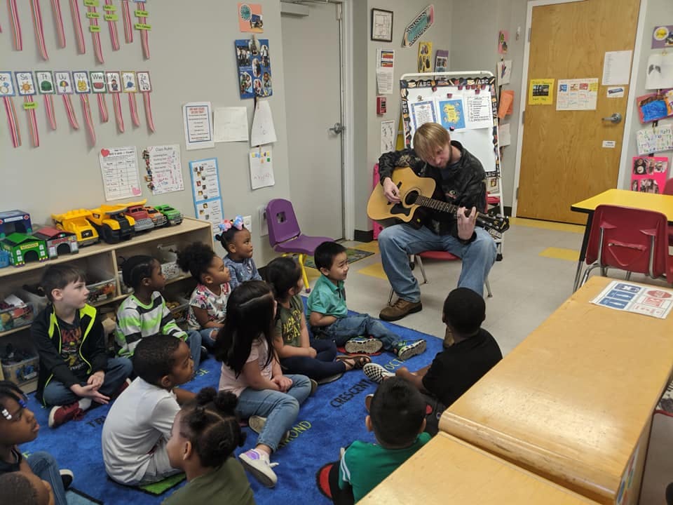 Person playing guitar for children in a classroom