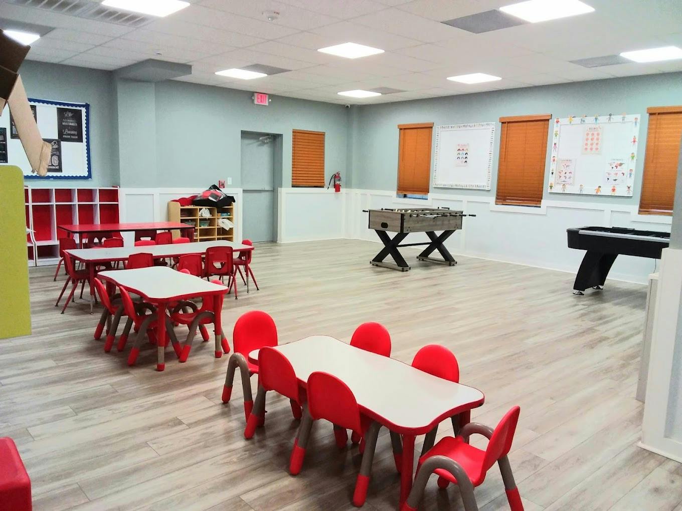 Classroom with small red tables and chairs, foosball table, and pool table