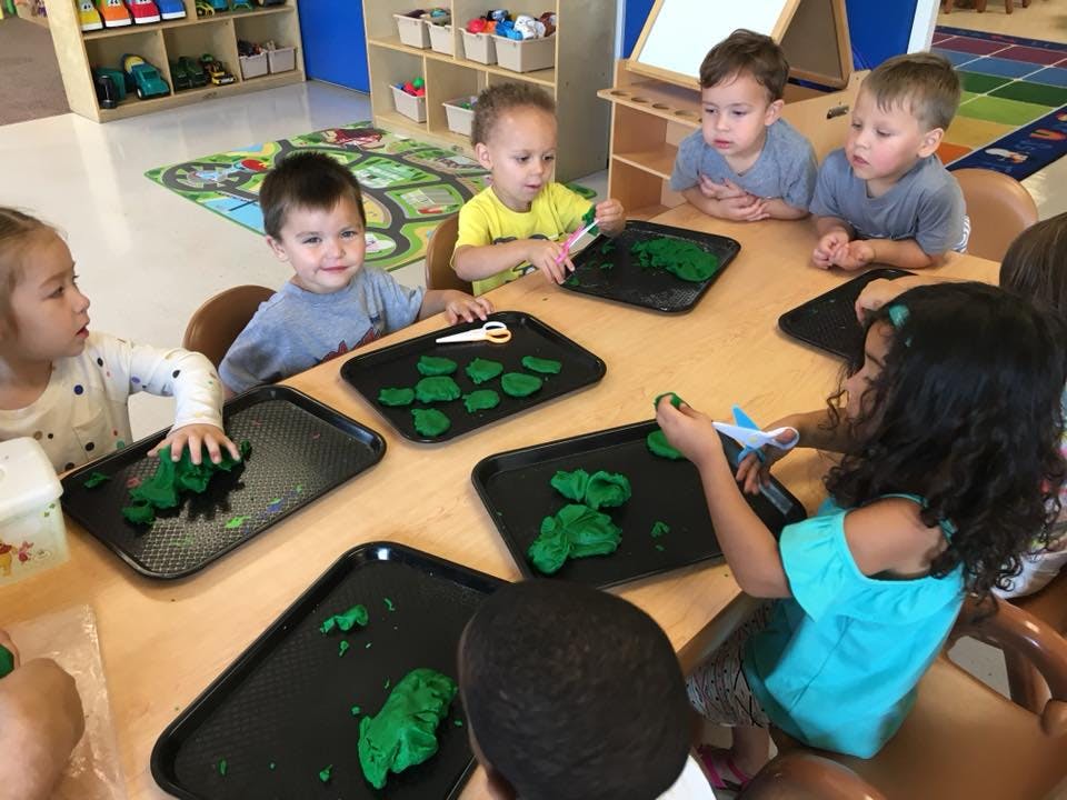 Children sitting around a table playing with green playdough