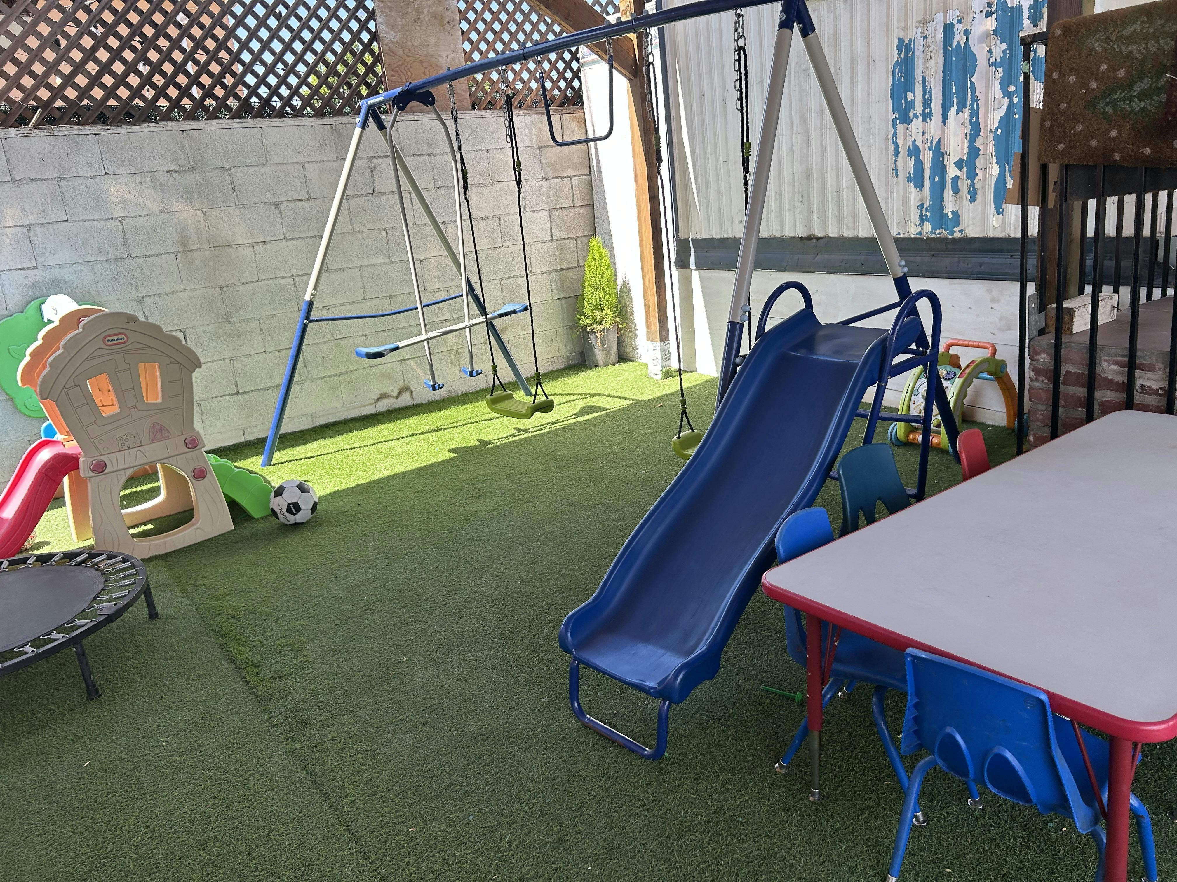 Outdoor playground with a blue slide, swings, and a small trampoline