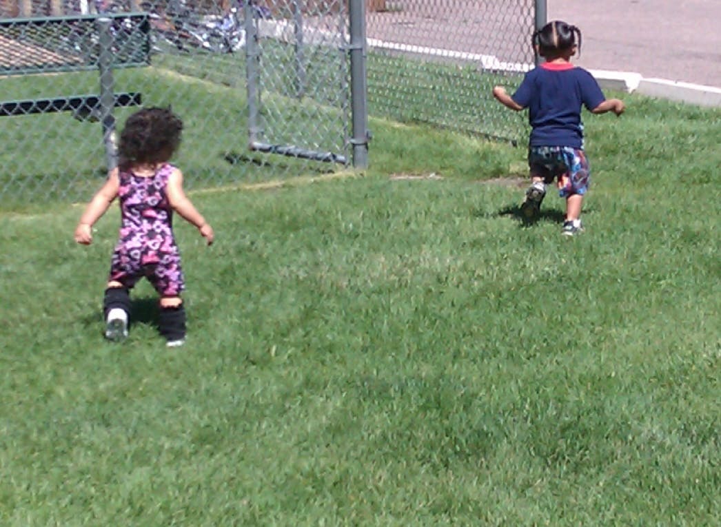 Two children running on grass near a fence