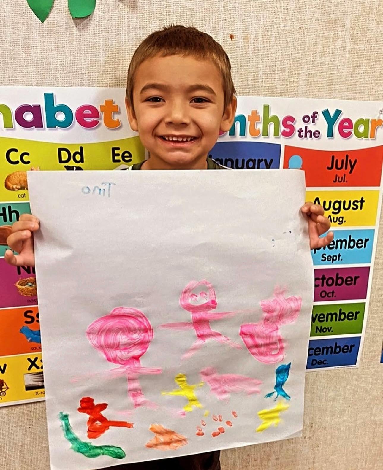 Child holding up a paper with a colorful painting in a classroom