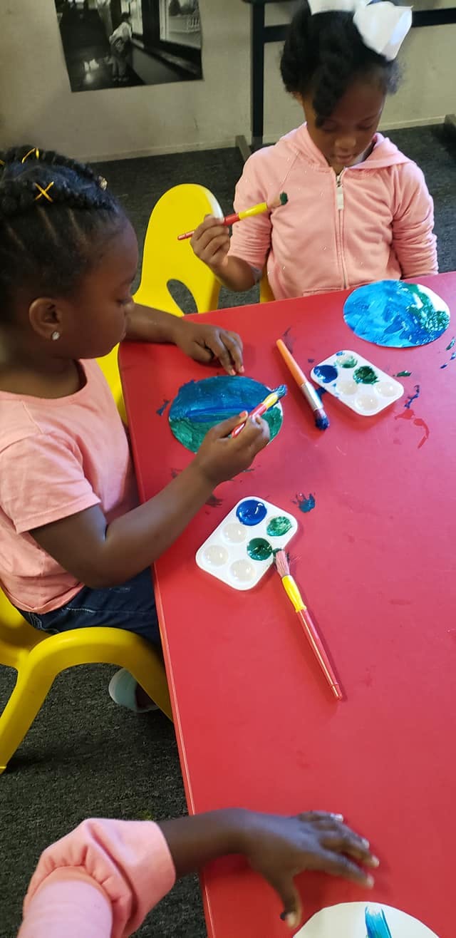 Two children painting at a red table with paint palettes and brushes