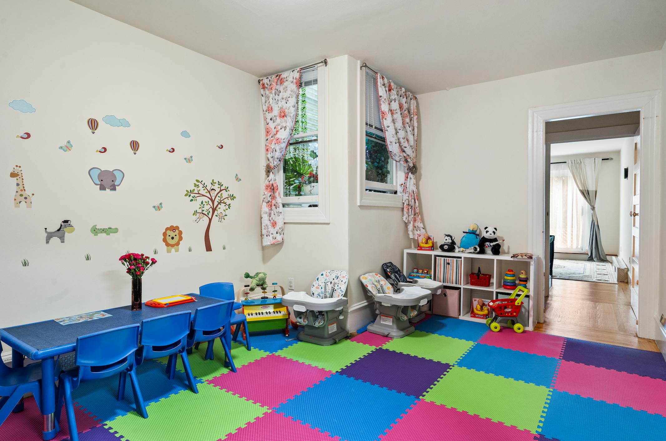 Playroom with colorful floor mats, small blue tables and chairs, and wall decals