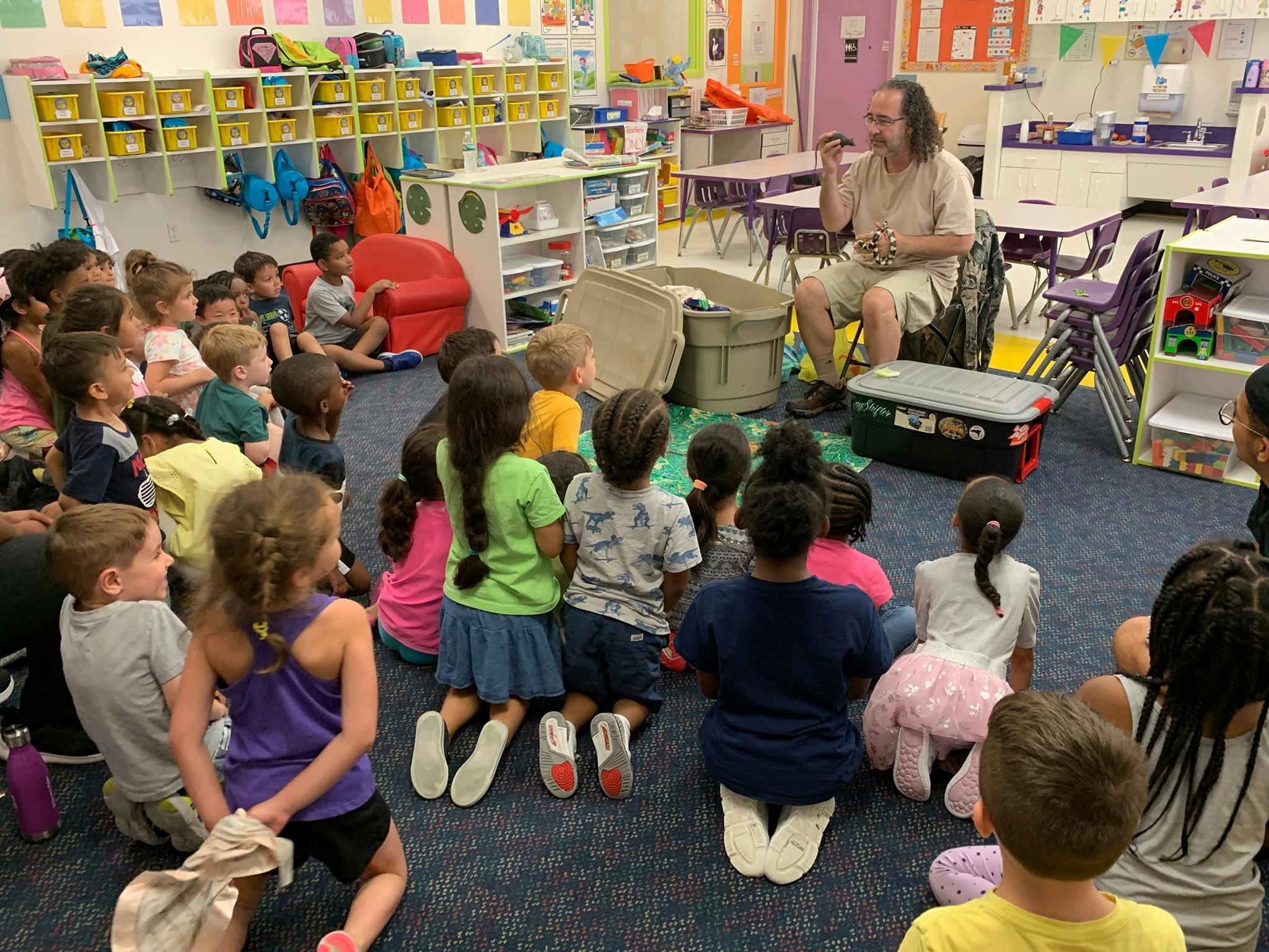 Adult person sitting in a chair talking to a group of children in a classroom