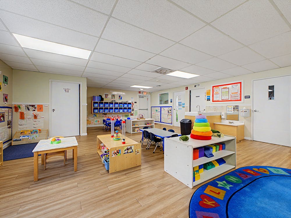 A colorful preschool classroom with small tables, chairs, and play equipment