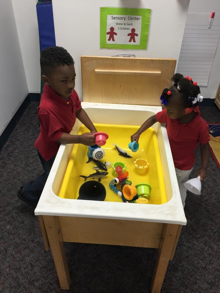 Two children playing at a sensory table with water and toys