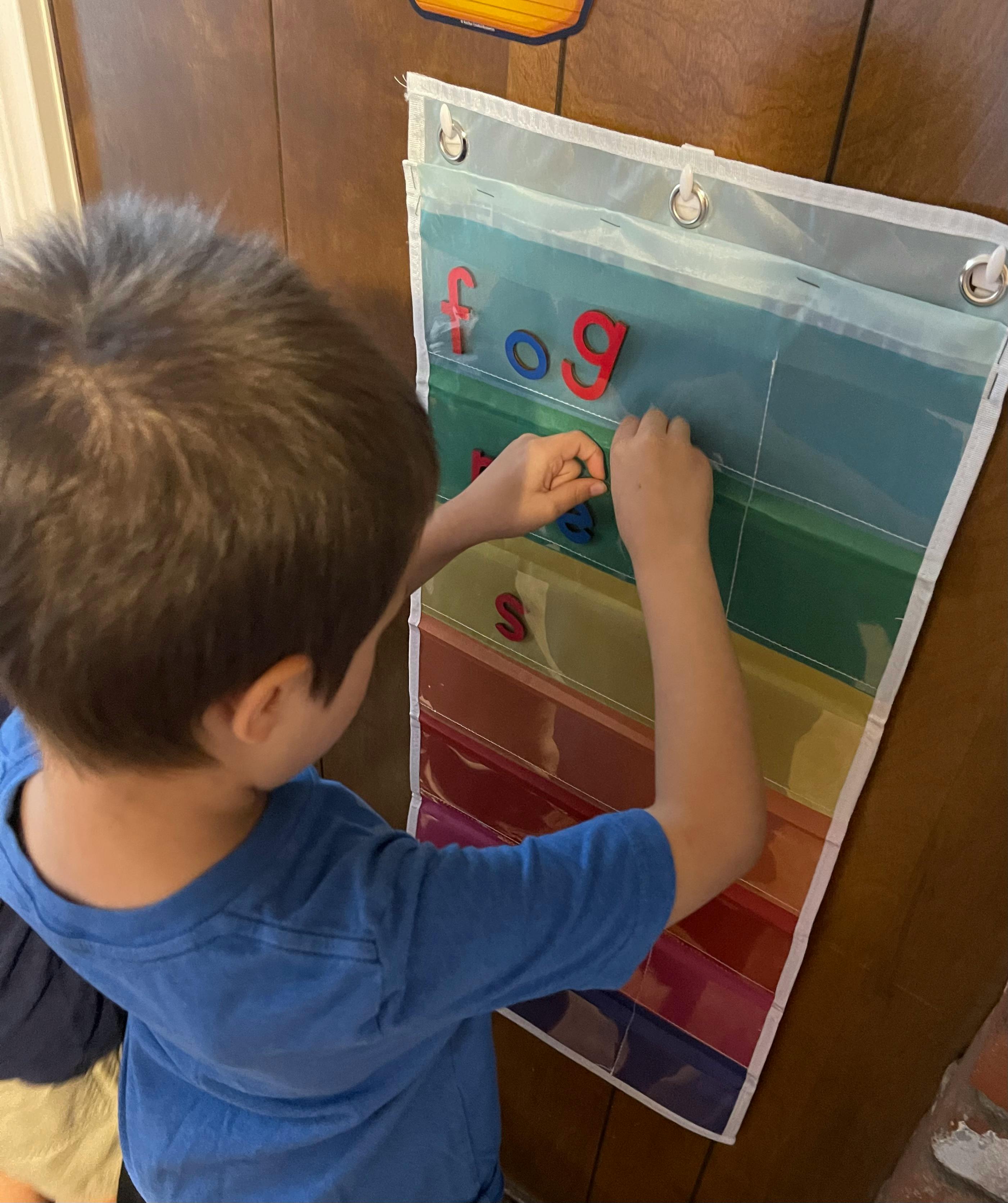Child placing letters on a rainbow-colored pocket chart