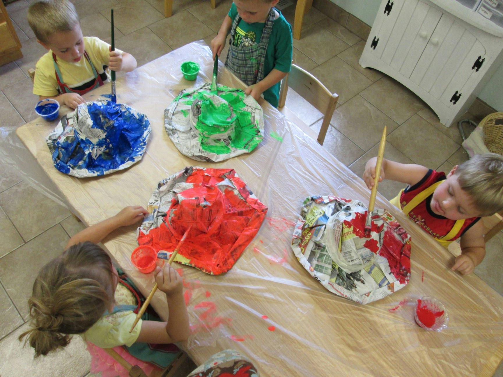 Children painting paper mache volcanoes at a table