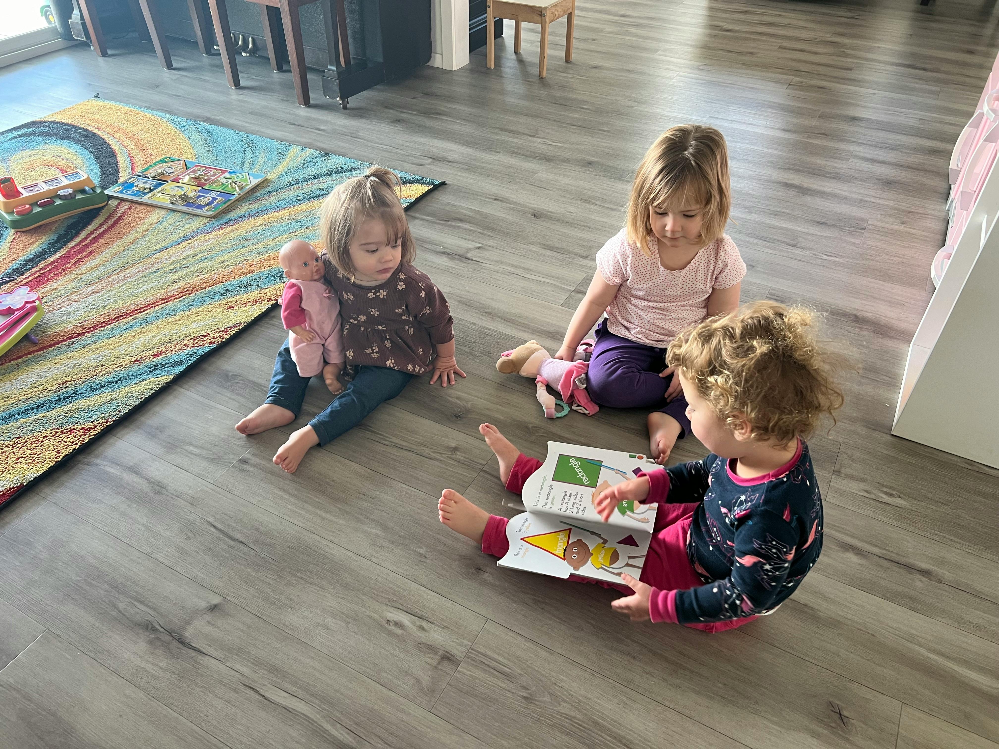 Three children sitting on a floor, one reading a book