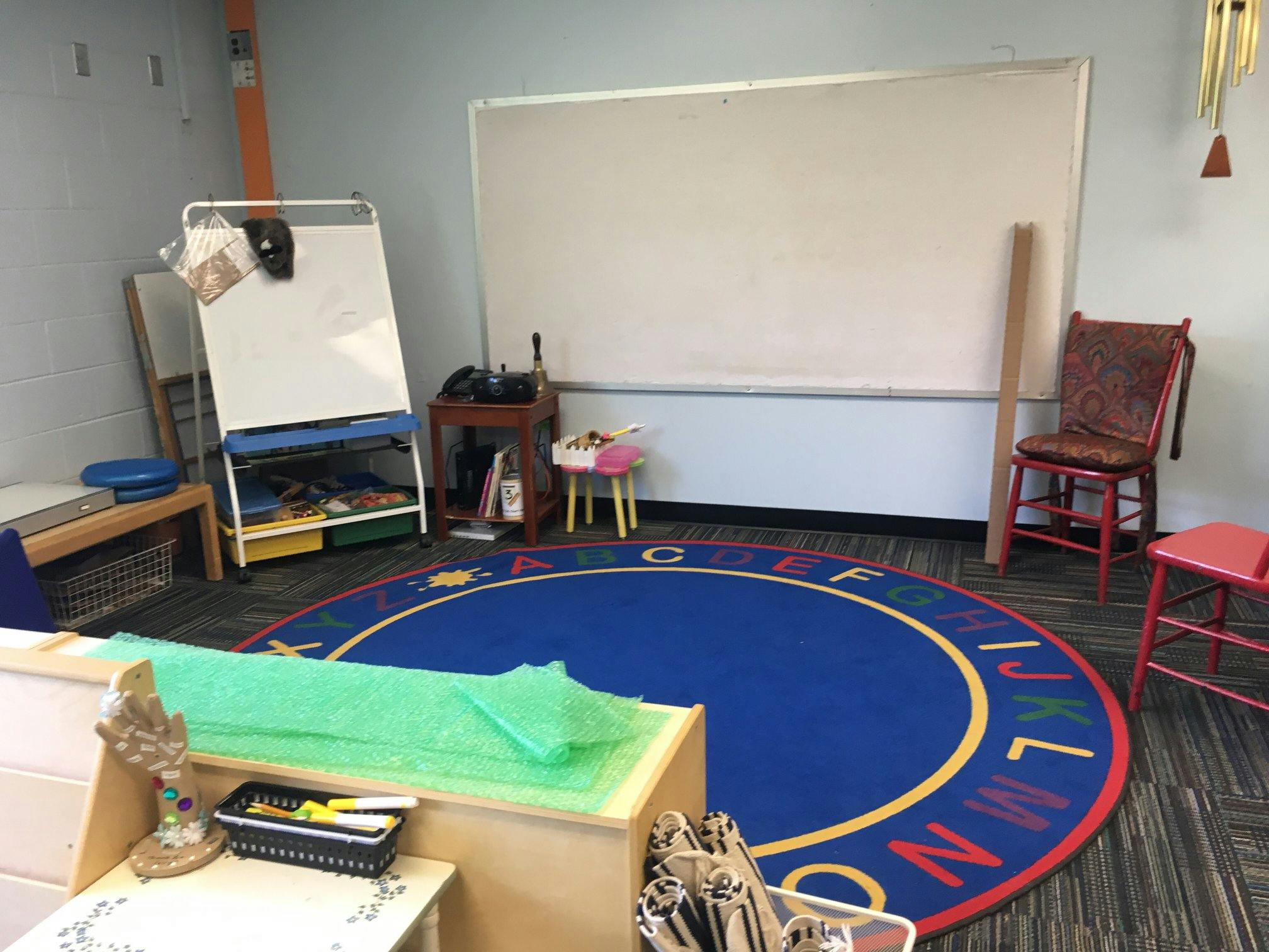 Classroom with a blue alphabet rug, whiteboard, and easel