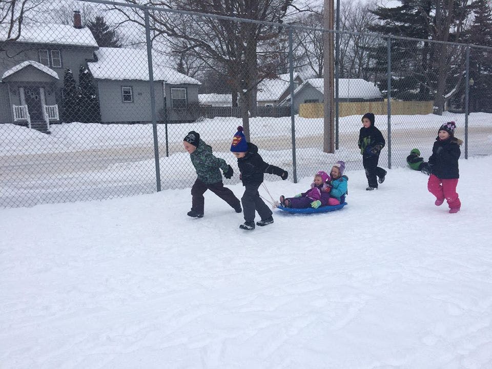 Children playing in snow, pulling a sled with two children on it