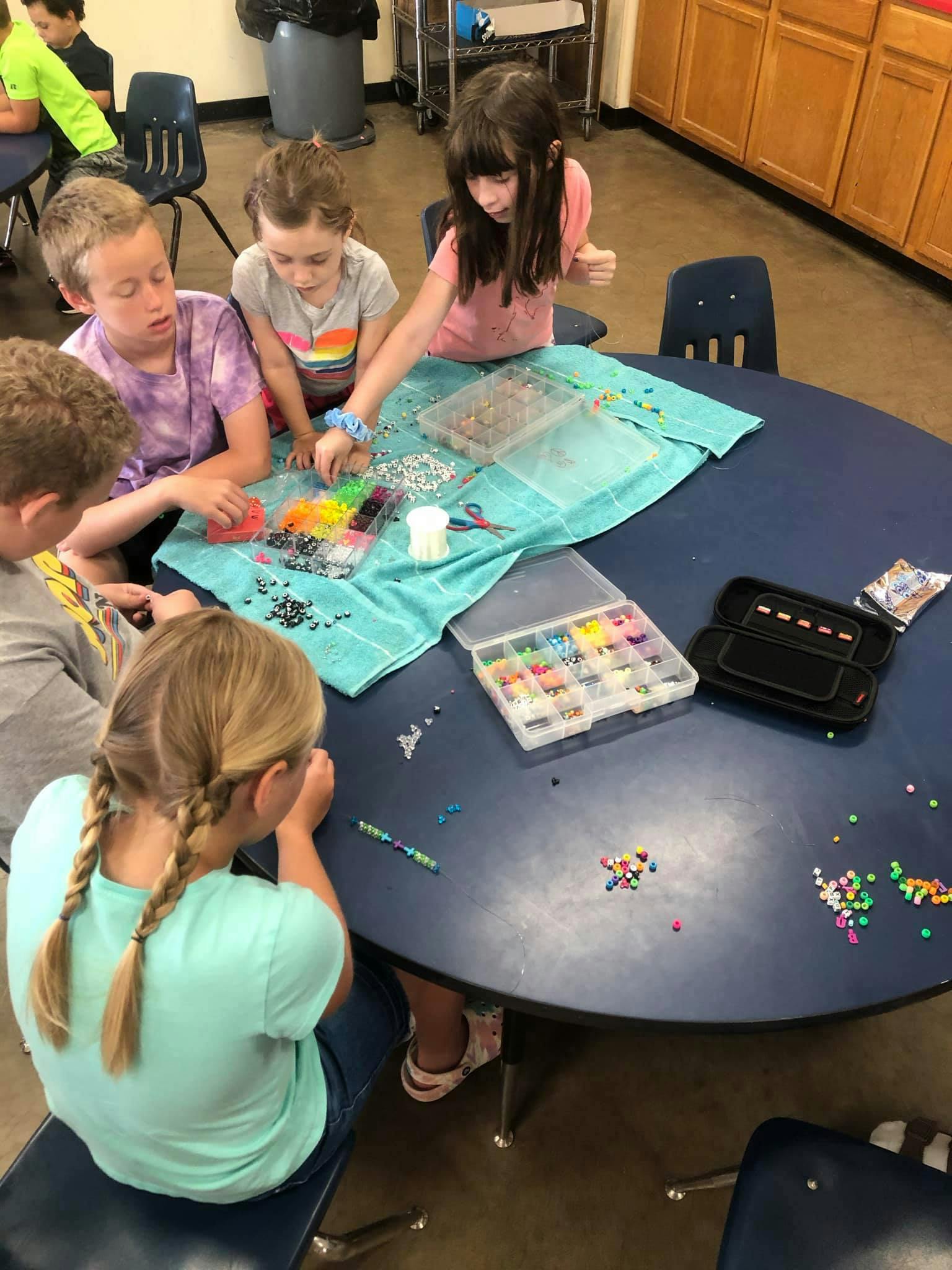 Children sitting around a table making crafts with beads