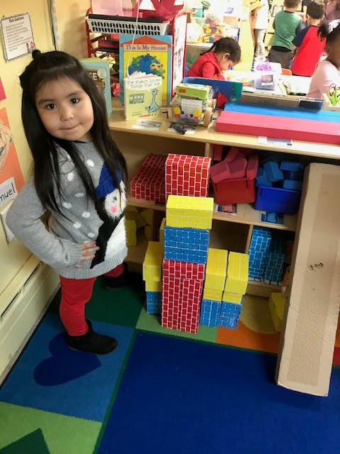 Child standing in a classroom next to shelves with blocks