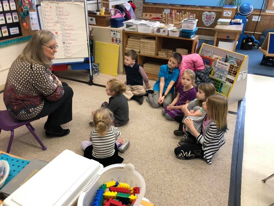 Adult and multiple children sitting on the floor in a classroom