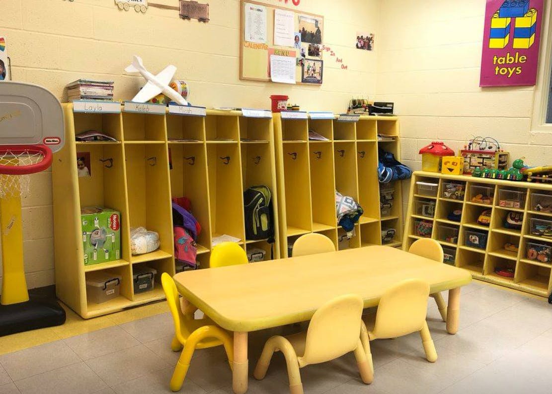 Classroom with small yellow table and chairs, cubbies, and toy shelves