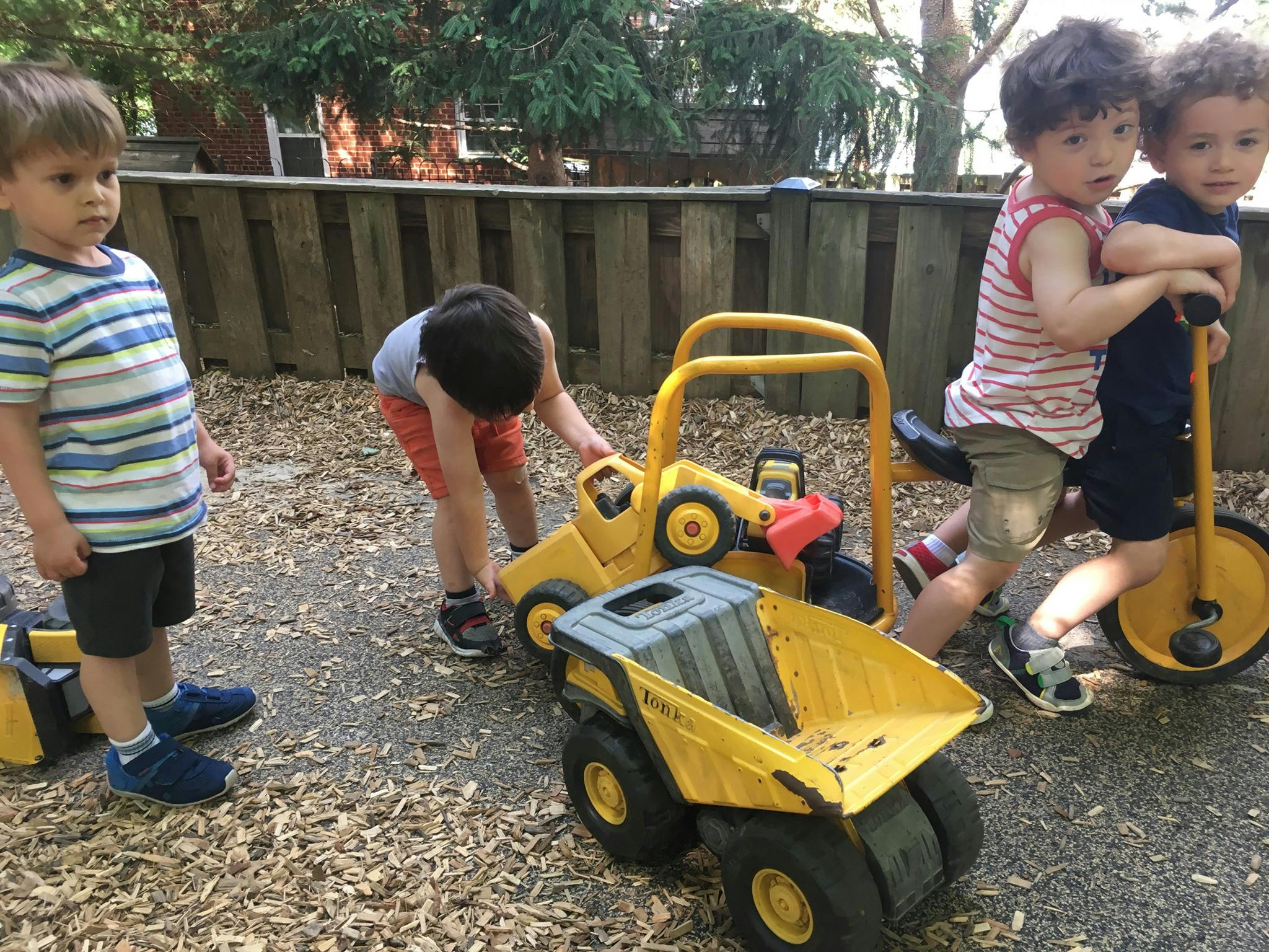 Three children playing with toy construction vehicles and a scooter outdoors