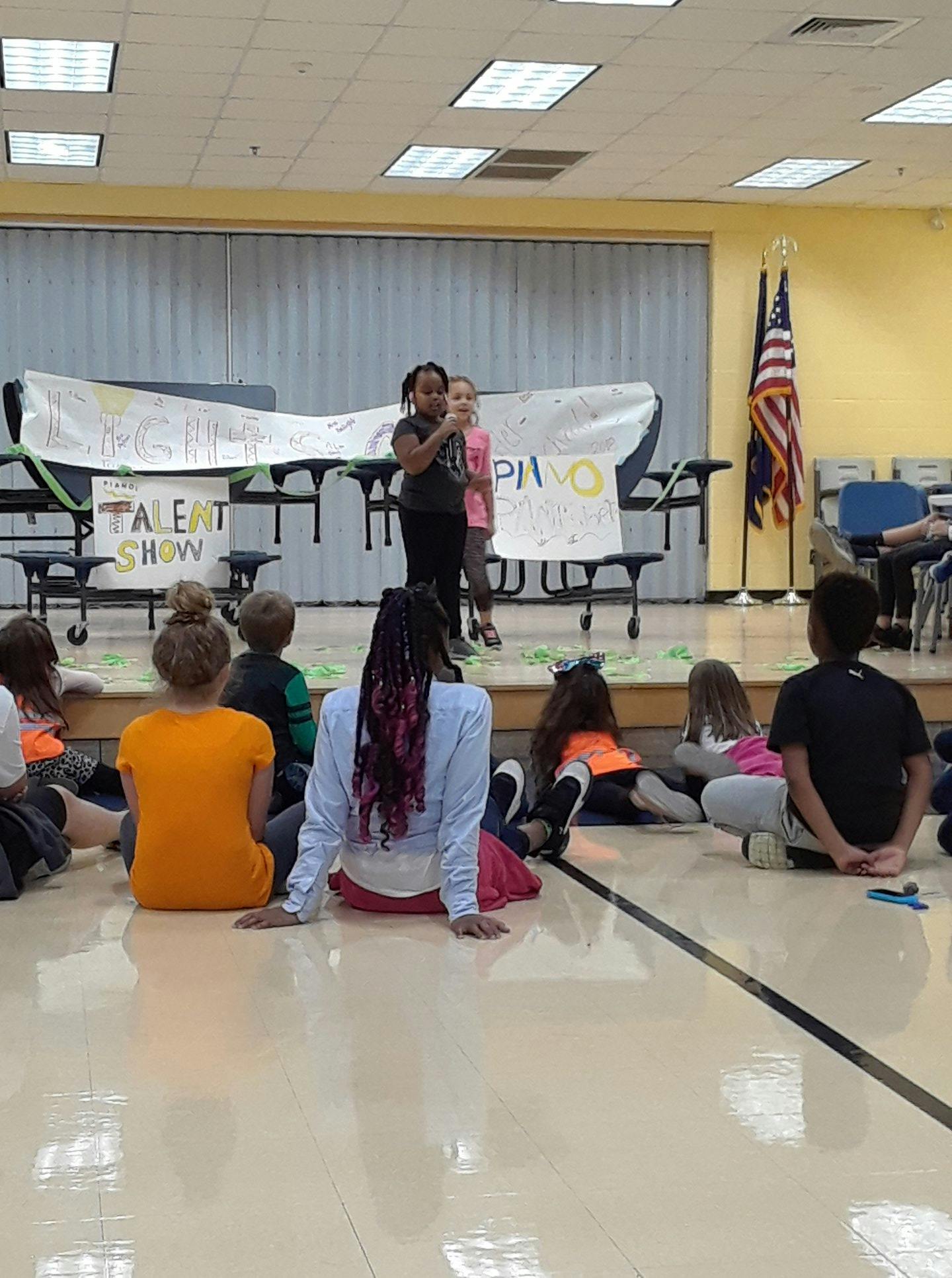 Children performing on a stage for an audience of children sitting on the floor