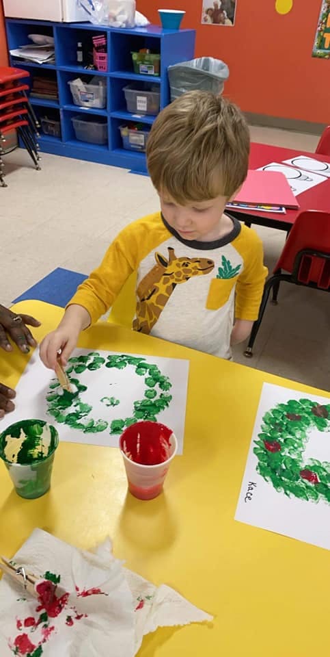 Child painting a green wreath on paper