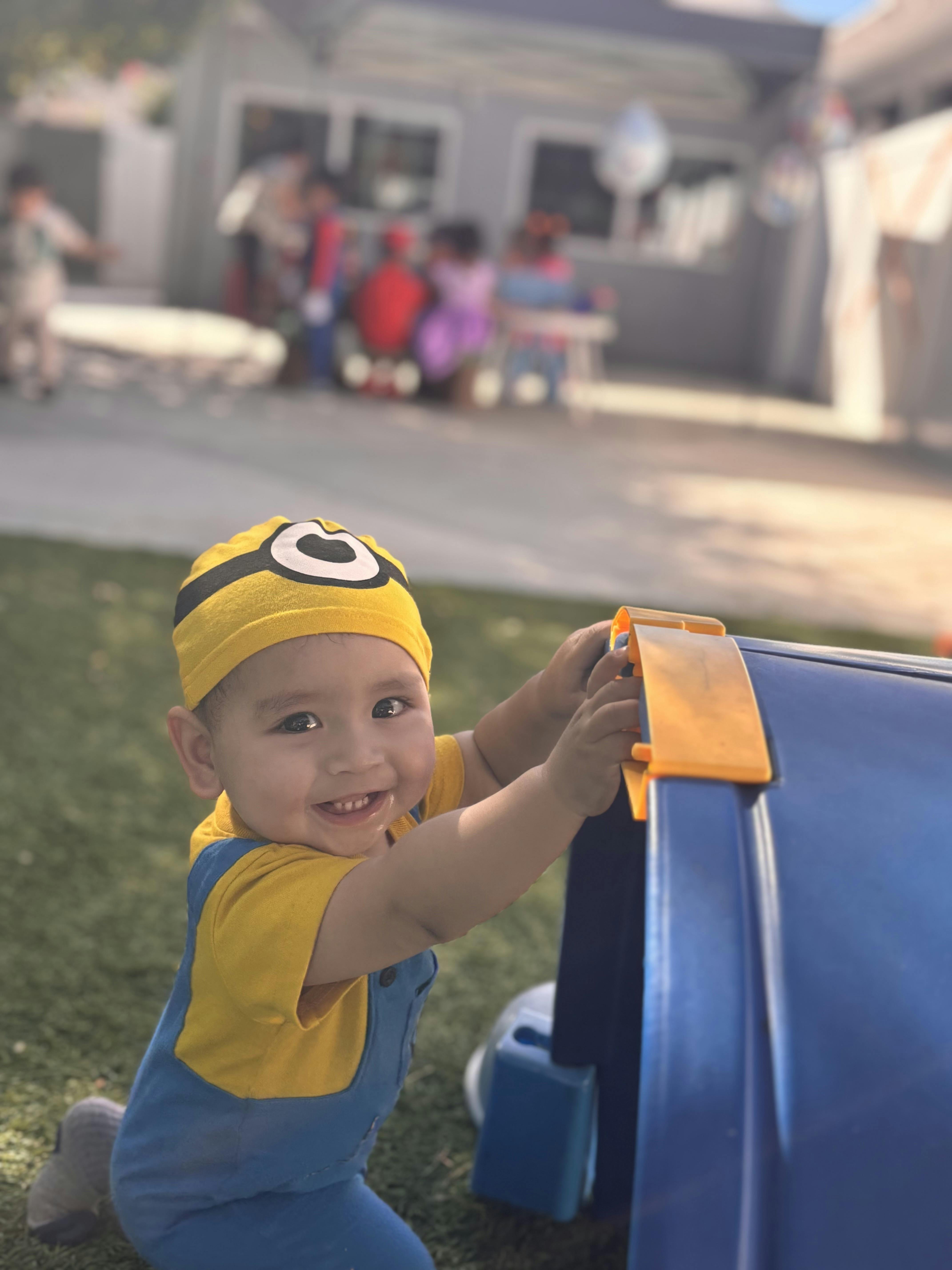 Child in yellow hat and blue overalls playing with a blue toy