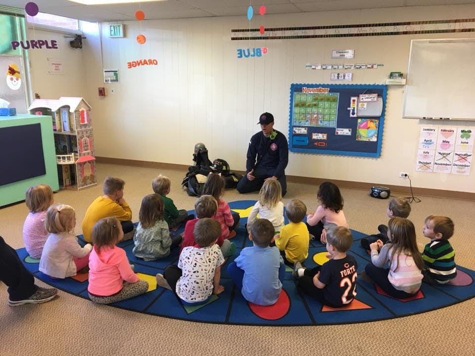 Adult speaking to a group of children sitting on a mat in a classroom