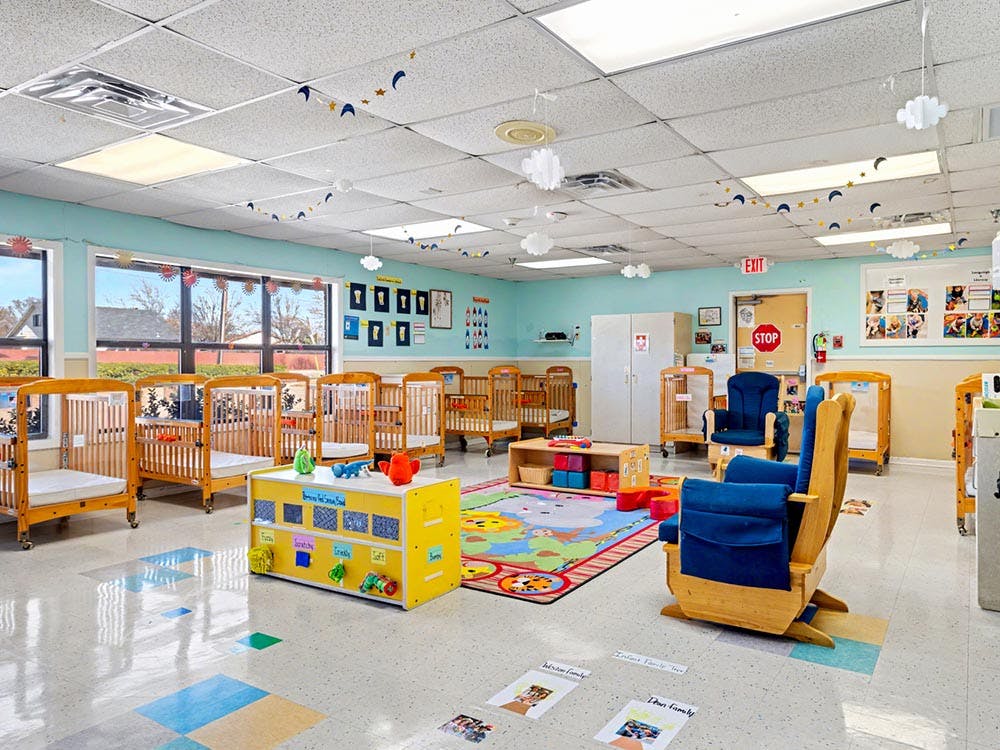 Classroom with multiple cribs, a play mat, and rocking chairs