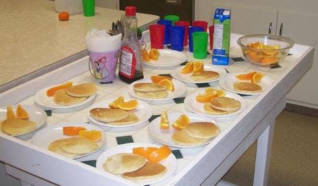 Plates of pancakes and orange slices on a table