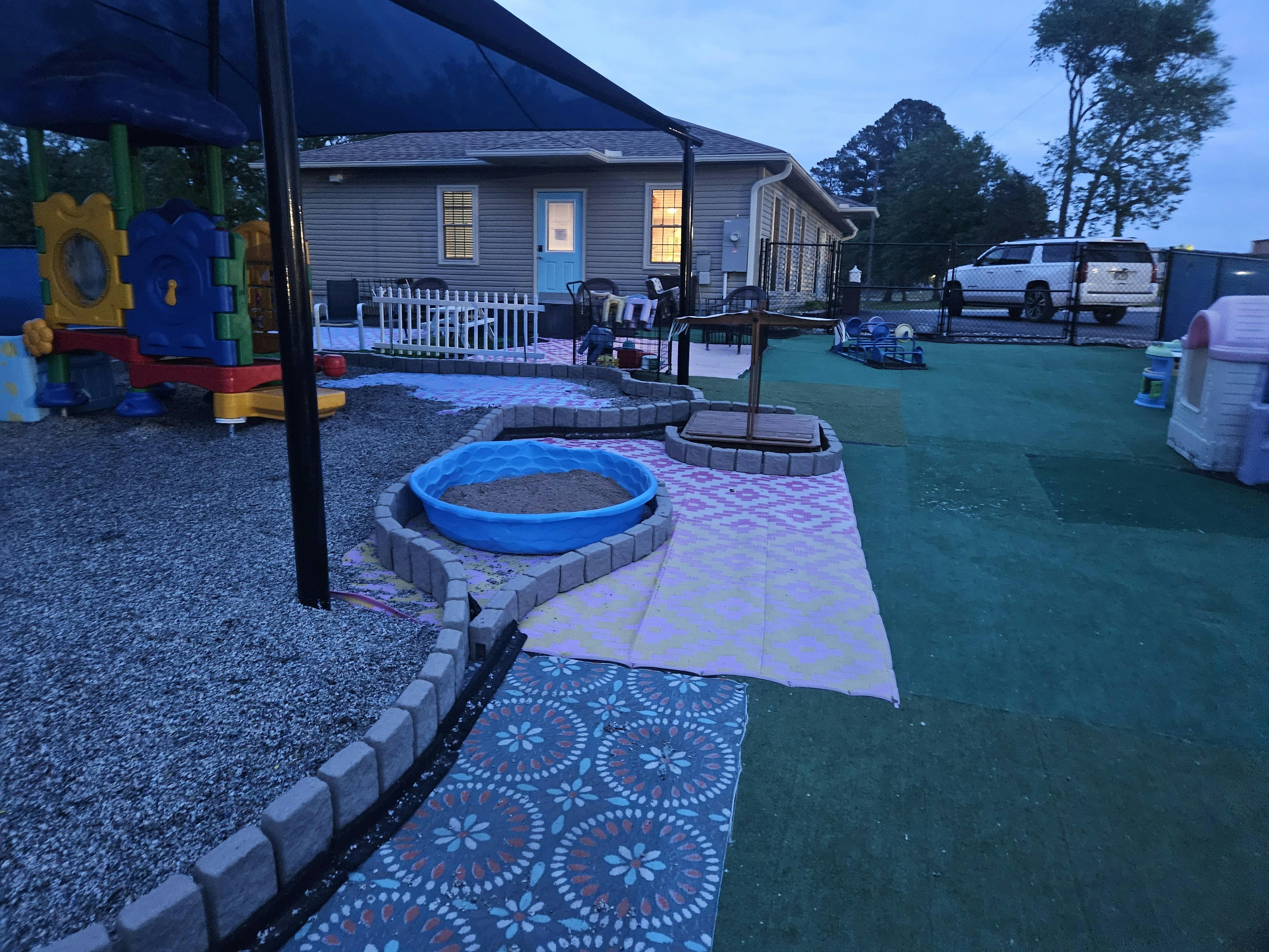 Outdoor play area with a sandbox, colorful play equipment, and a small house