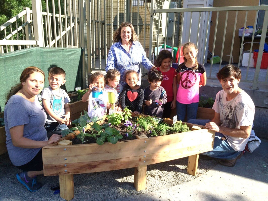 Adults and children gathered around a raised garden bed